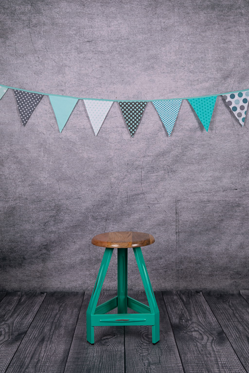 grüner Stuhl vor grauem Foto-Hintergrund mit bunter Wimpelkette